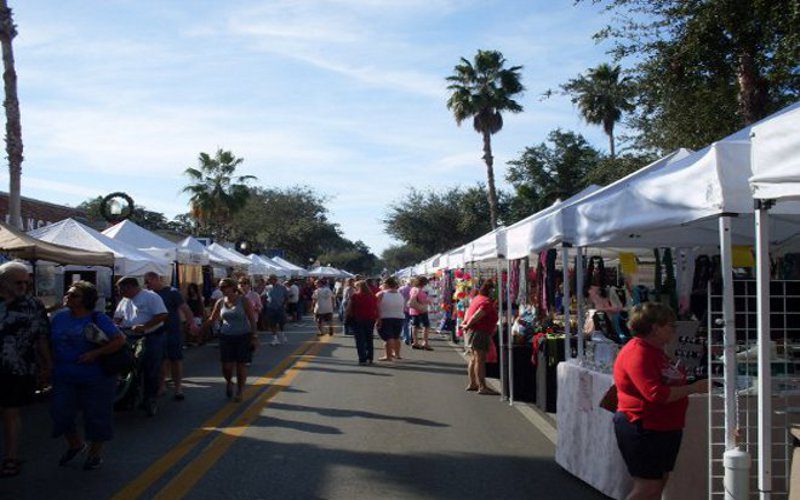 Outdoor market with white tents and people shopping on a sunny day.